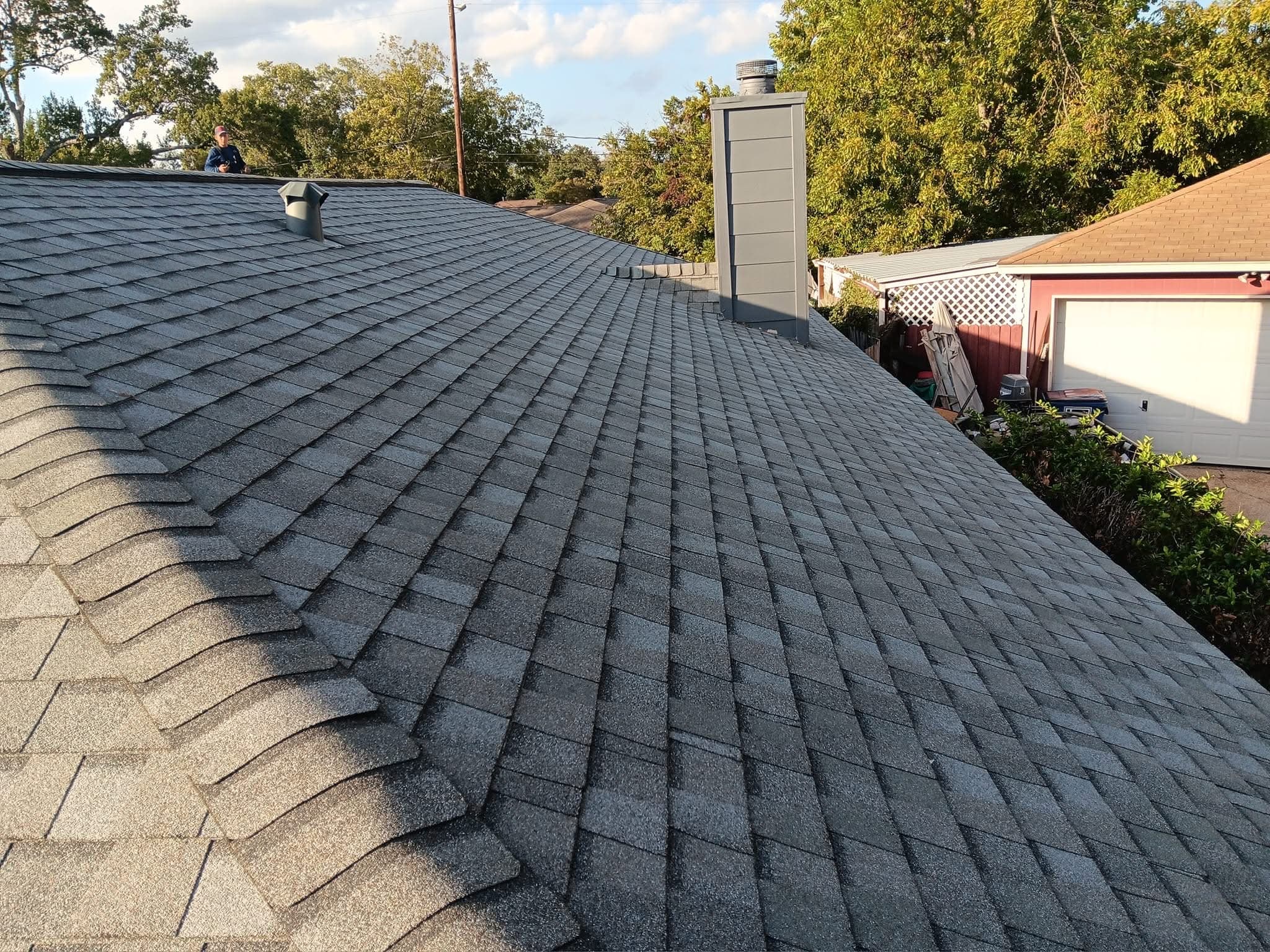 Freshly installed gray architectural shingle roof with brick chimney